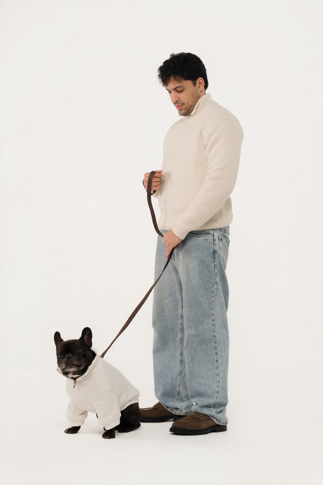 Tutor de tricô off-white segurando a guia de couro do seu buldogue francês de moletom